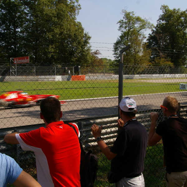 Zuschauer vor Zaun und Formel 1 Auto im Hintergrund
